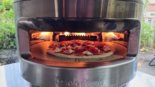 The Solo Pi sits on a counter outside. There's fire in the back of the oven and a pizza inside.