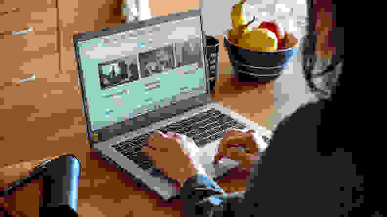 A person types on a laptop next to a bowl of fruit