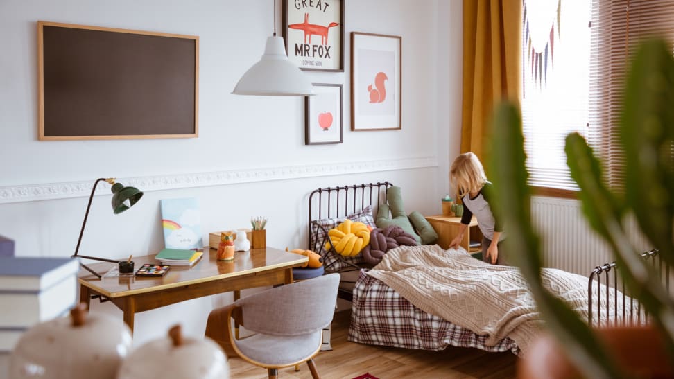 A kid's bedroom seen with a desk and a bed being made up.