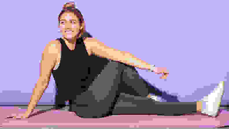 A person stretching in the Wolaco grey leggings and Clinton Muscle Tank.