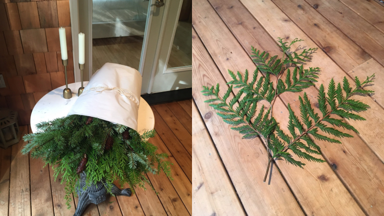 On left, evergreen foliage on small table next to white candles on gold candlesticks. On left, two pieces of evergreen foliage on wooden floor.