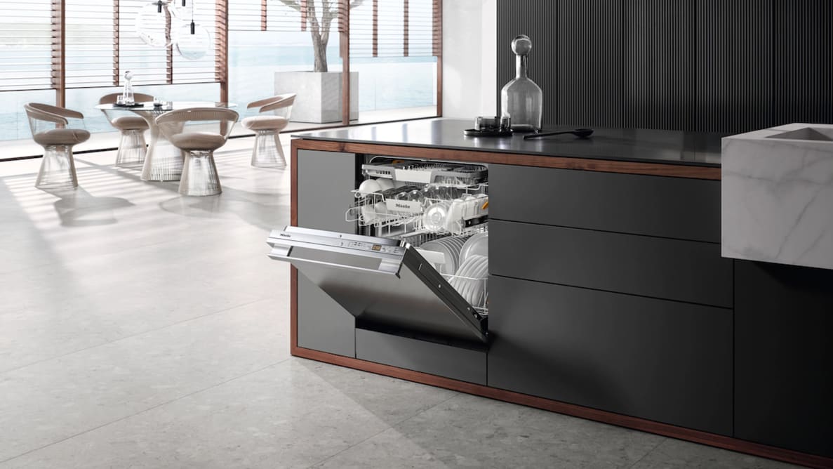 An image of a modern kitchen that includes the Miele dishwasher. Its door is open, revealing its inner racks stocked with spotless dishes.
