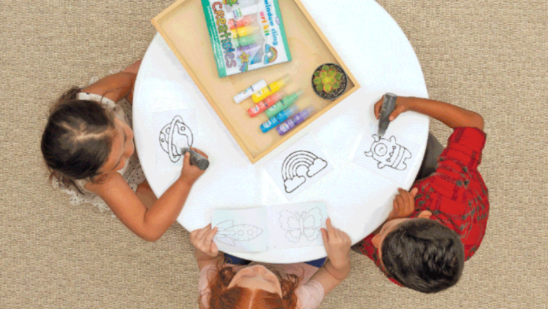 Three kids sitting at a table creating window art