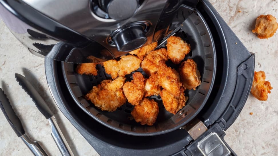 Shot from above of an air fryer, with its basket pulled out revealing a batch of fried chicken.