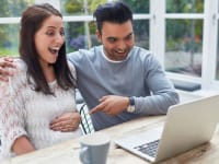 A pregnant woman and man sitting at an outdoor patio table using the computre
