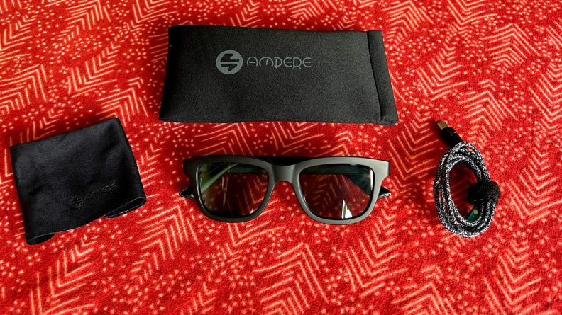 Sunglasses sit on a red background with a shammy, case, and charging cable.