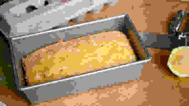 The USA Pan with a loaf of lemon pound cake is next to a carton full of eggs and a halved lemon.