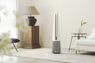 A tall, silver, needle-like air purifier stands in a modern living room