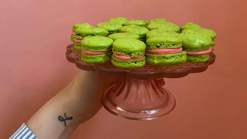 A hand holds a pink cake stand filled with lime green macarons.
