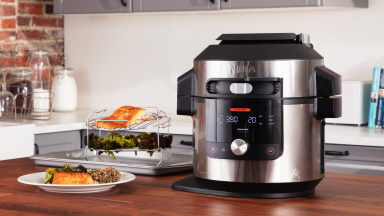 A Ninja Foodi pressure cooker sits on a kitchen countertop surrounded by food.