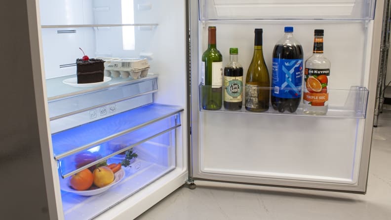 A close-up on the bottom half of the fridge compartment and its door. Both the crisper and door bin are stocked with food, and you can see the blue glow coming from its crisper LED.