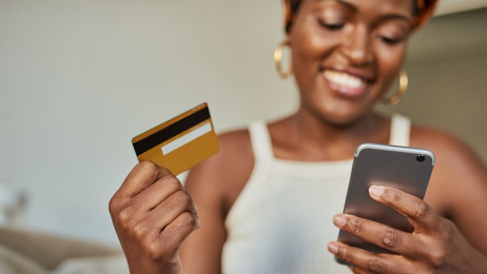 Smiling person holding cell phone in one hand and credit card in the other