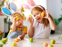 Brother and sister wearing bunny ears playfully hold up colored Easter eggs