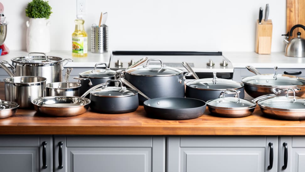 Three complete cookware sets are lined up on a kitchen island