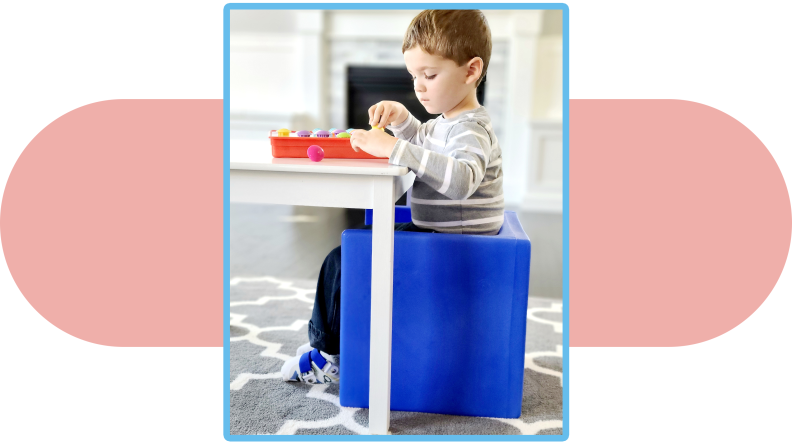 A child sits on a cube chair and plays with a game on a table.