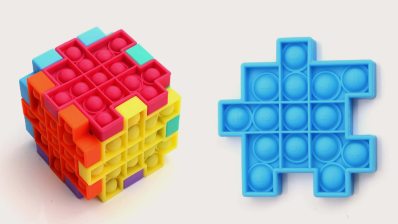 a colorful, cube-shaped pop-it created with 6 different pop-its, next to a blue, single pop-it