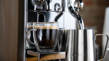 A close-up photo of the Breville Nespresso Creatista brewing an espresso shot and frothing milk.