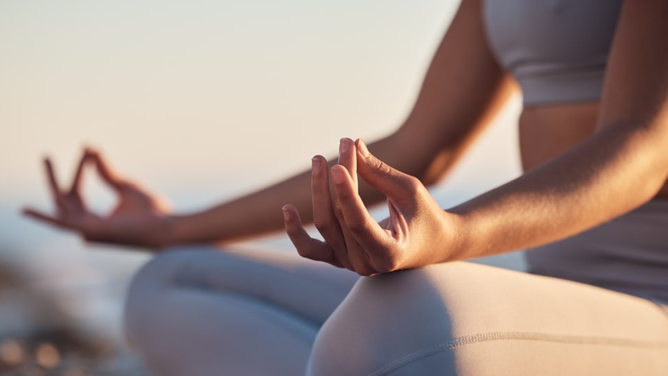 Closeup of woman meditating with hands in lotus pose meditation at a beach at sunset