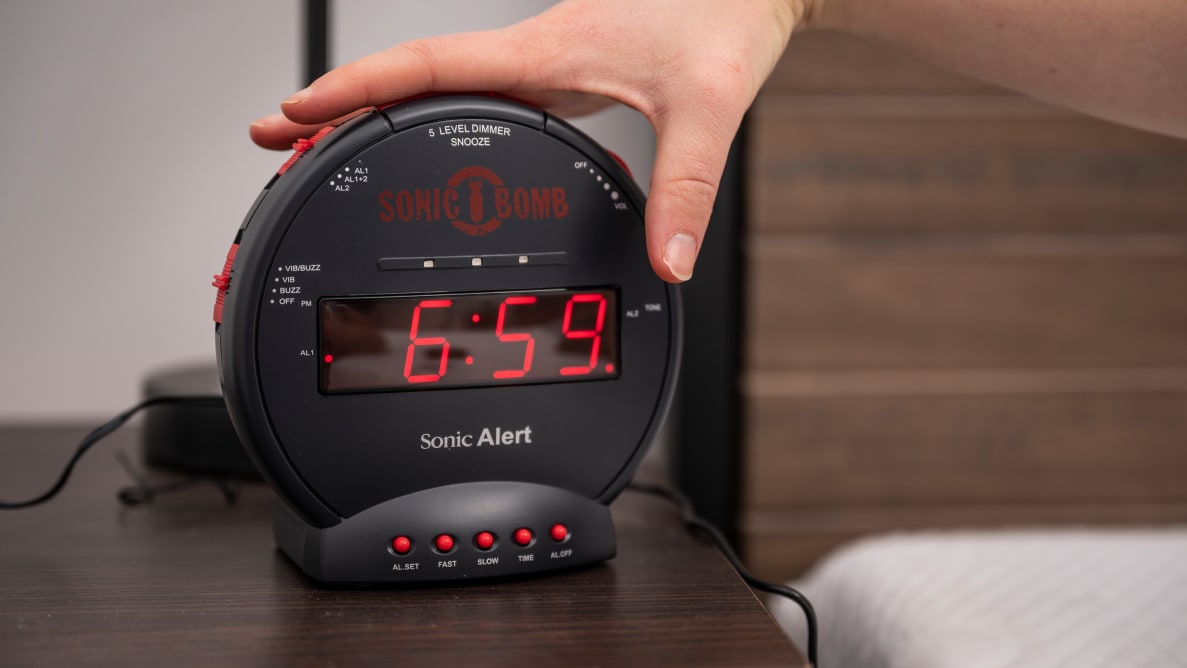 a person's hand presses the snooze button on the sonic bomb alarm