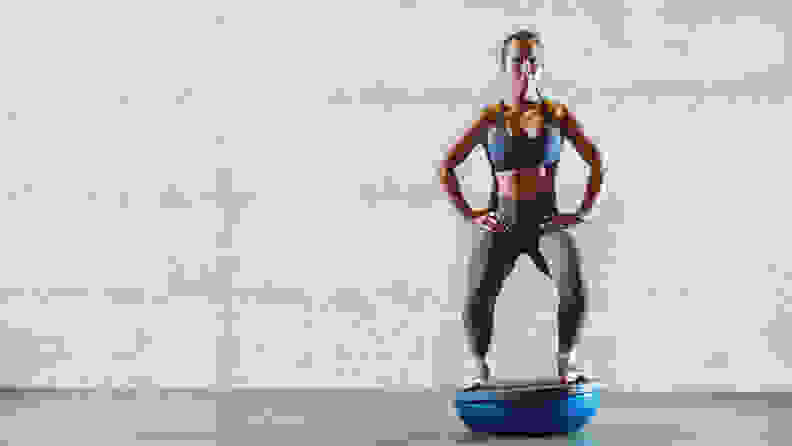 A woman squatting on the flat side of a BOSU ball.