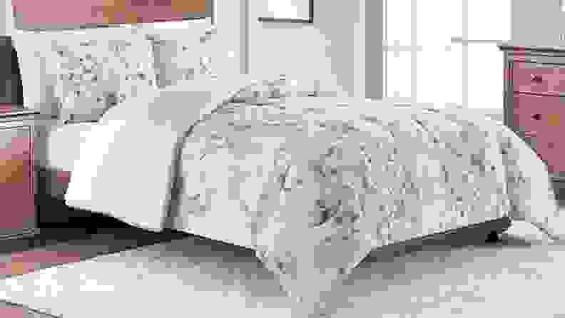 A bed is neatly made. The comforter is adorned with a pink floral pattern.