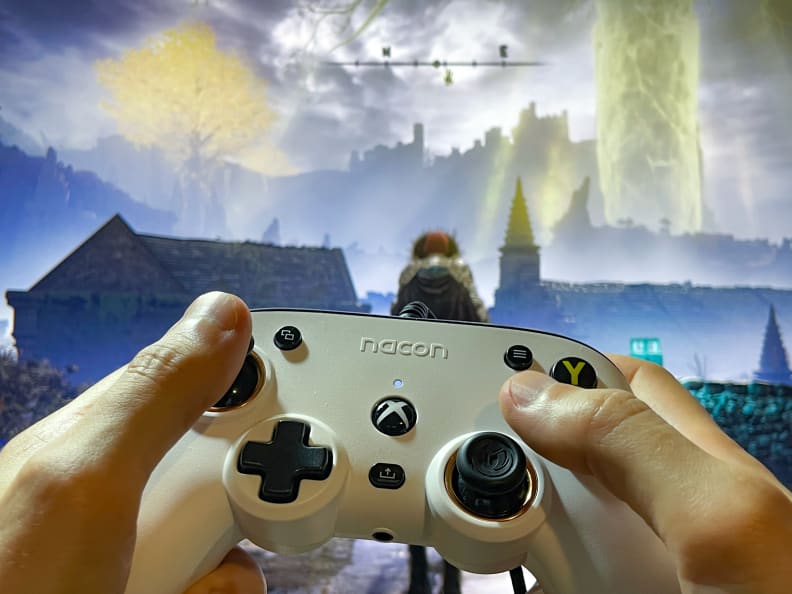 A pair of hands holding the controller in front of a screen playing a video game.