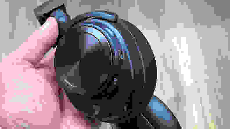 A hand holds the Arctis Nova Pro Wireless headset displaying the control buttons on an ear cup.