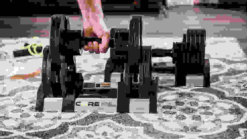 A hand lifting a pair of adjustable dumbbells out of their tray.