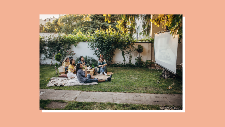 A group of friends sitting outside waiting to see a movie on a projector screen.