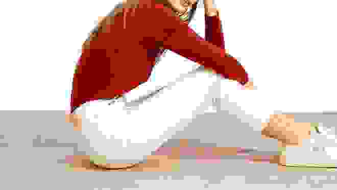 Woman sitting in white capri pants, a red long-sleeve shirt and white sneakers
