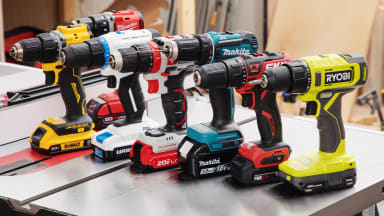 Six cordless drills from brands like Ryobi, Makita, and others sitting on a table