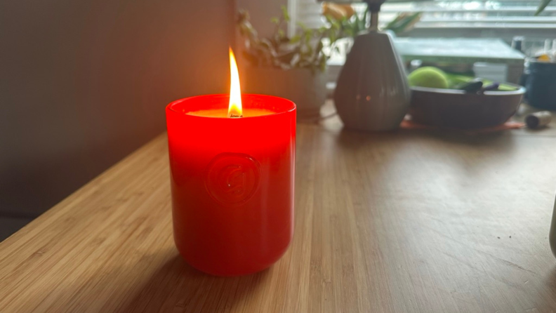 A Glossier You candle lit and on a table.