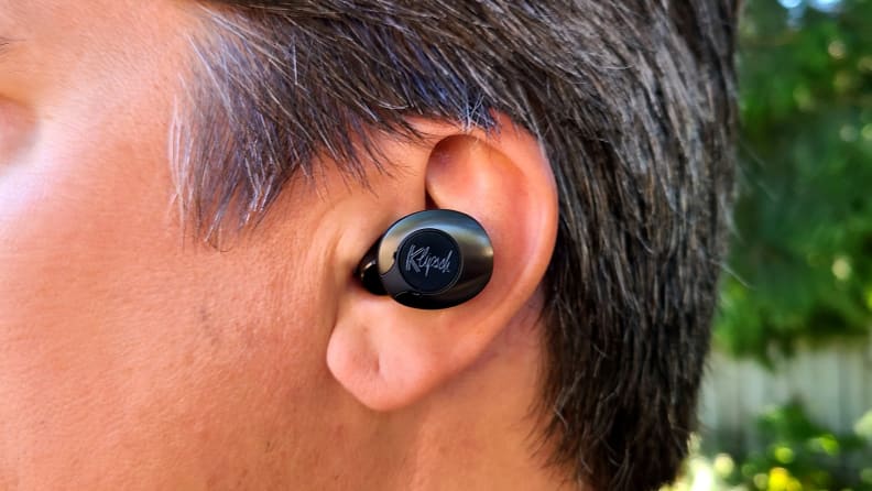 The black enameled Klipsch T5 II True Wireless ANC earbud sits in the ear of a man with salt and pepper brown hair.