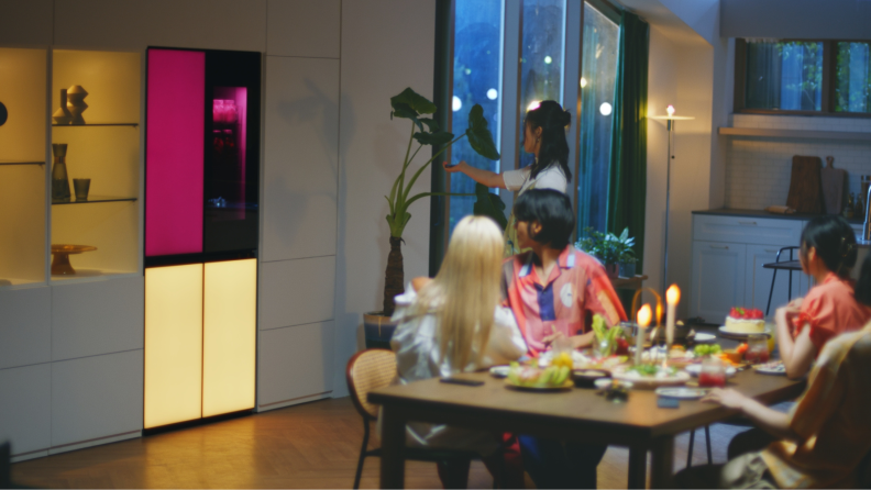 Group of friends sitting in kitchen at table while admiring the LG MoodUP refrigerator.