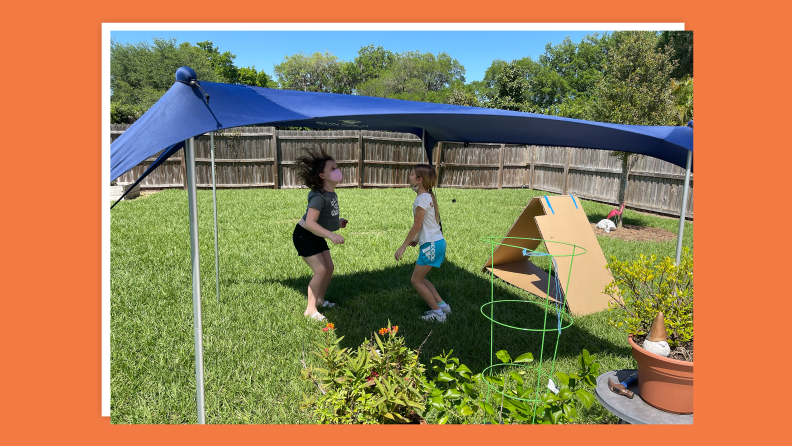 Two small children jump and play in shaded area under canopy.