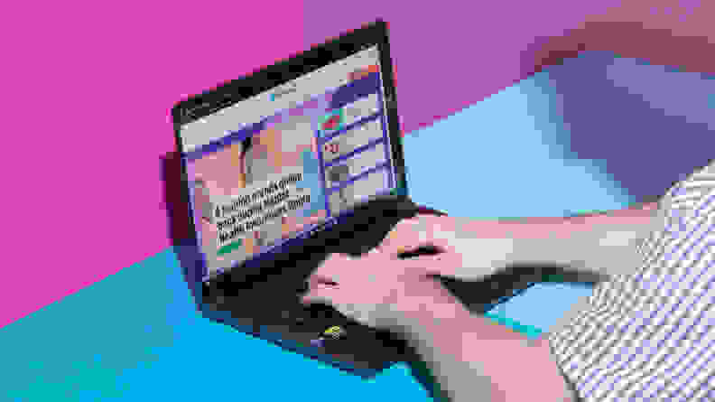 A person typing on the Acer Swift X 14 on a blue table with a pink background.