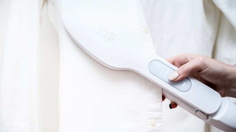 A person holding a travel iron selects a temperature setting