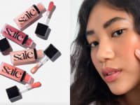 On the left: The four Saie Dew Blush colors with the applicators out of the tubes. On the right: A person holding two fingers up to their cheek to apply the Cloud Paint.