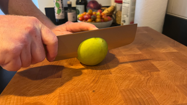 A Nakiri knife slicing a green apple in half on top of a wooden cutting board.