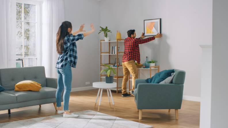 Man and woman measuring and hanging up wall art in living room