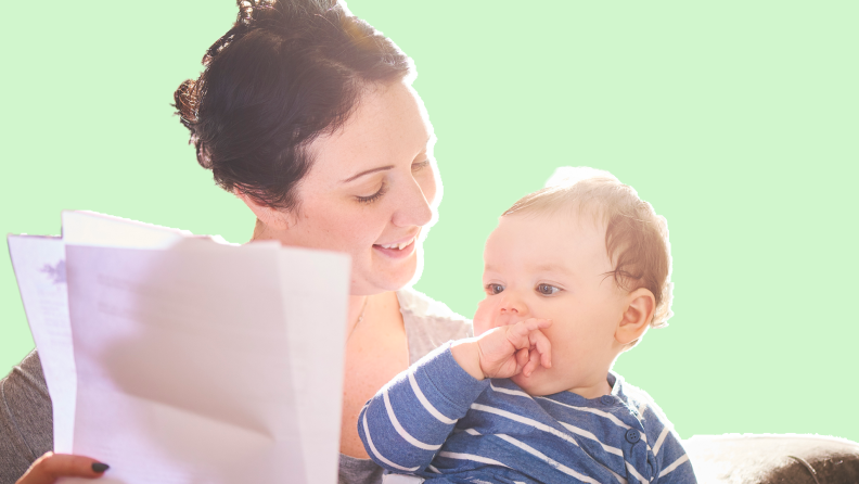 Small toddler with fingers in mouth sitting in smiling mother's lap while mother holds two forms in hand.