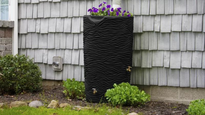 A black decorative rain barrel with plants planted on top.