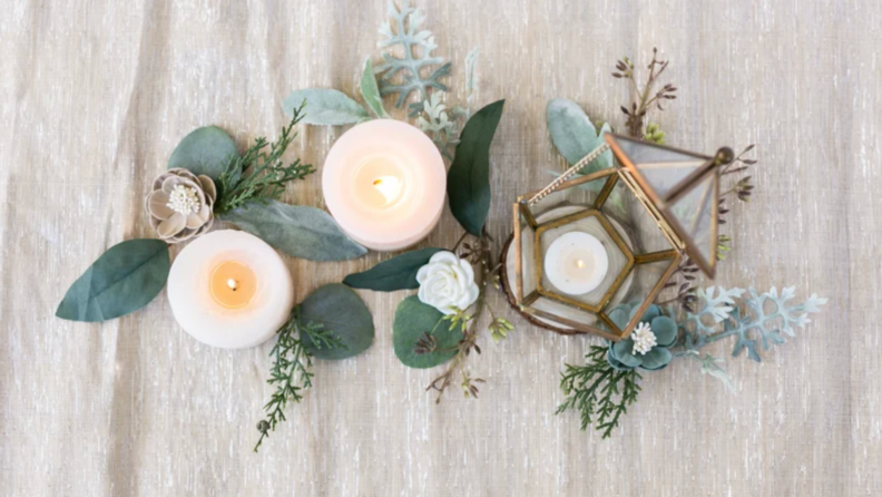 Eucalyptus plants mixed with white candles and lamp on table.