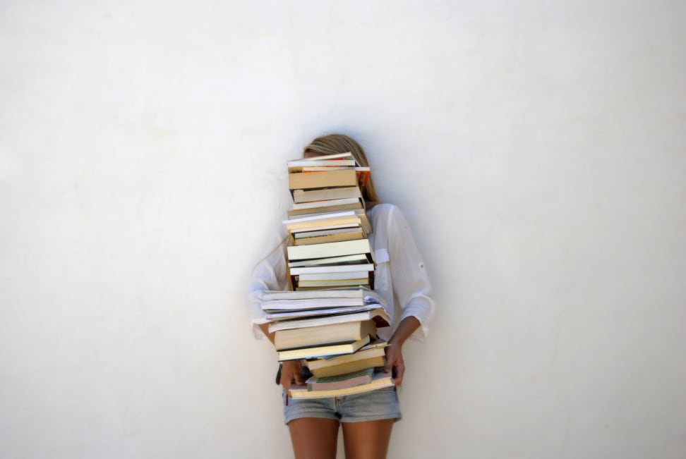 A woman carries a stack of books