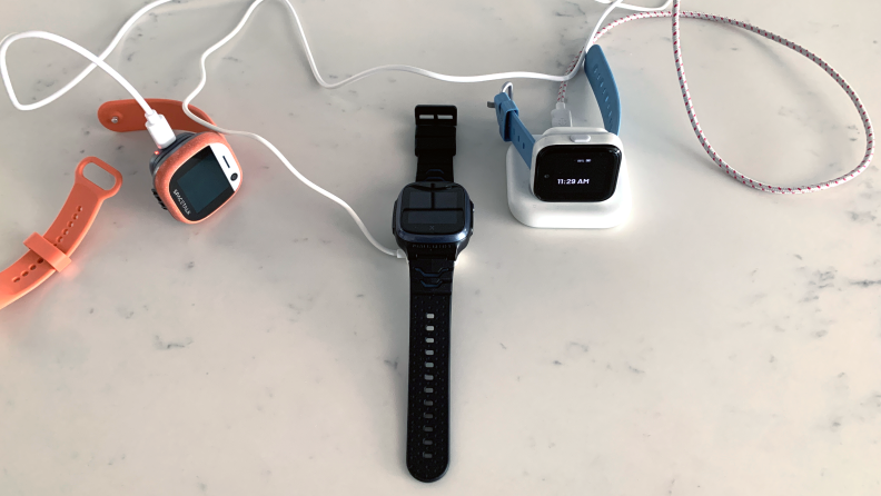 Three kids' smartwatches charging on a marble counter