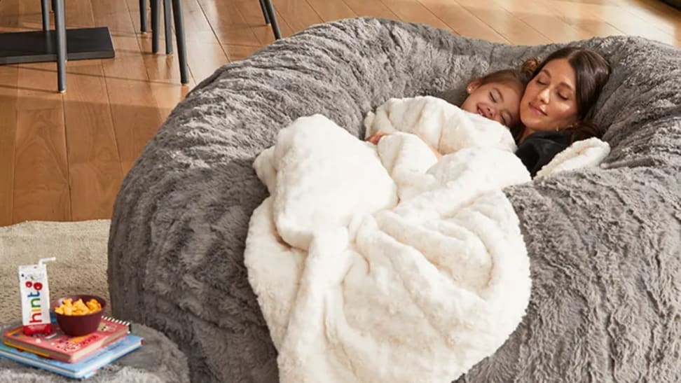 A mom and child cozy under a blanket on a Lovesac bean bag chair.