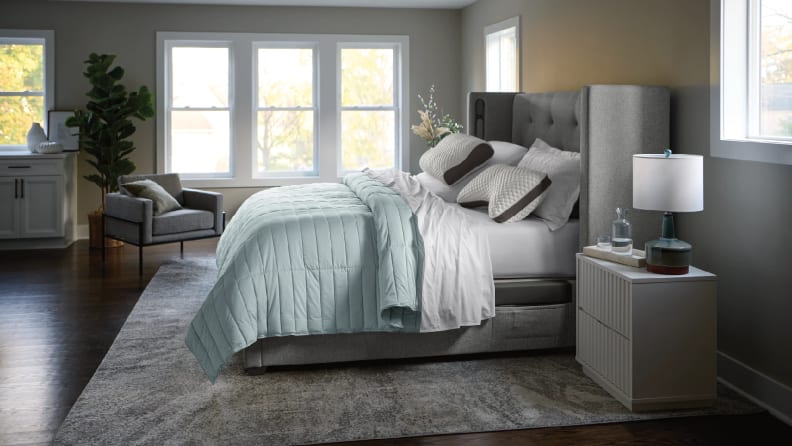Sleep Number bed with teal bedding and a grey wingback headboard in a room with three large windows.
