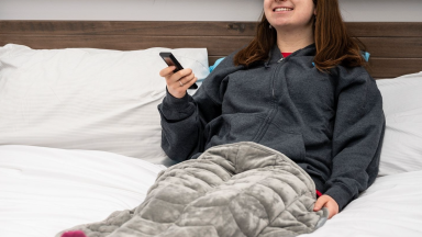 Woman laying on bed holding remote with grey blanket over her legs