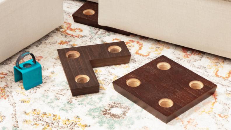 Steel clamp and wood blocks with holes for the couch feet sit on a rug in front of the Sactional.