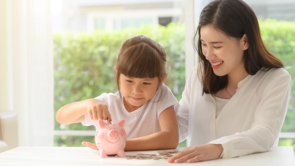 A child and parent put money into a piggy bank.